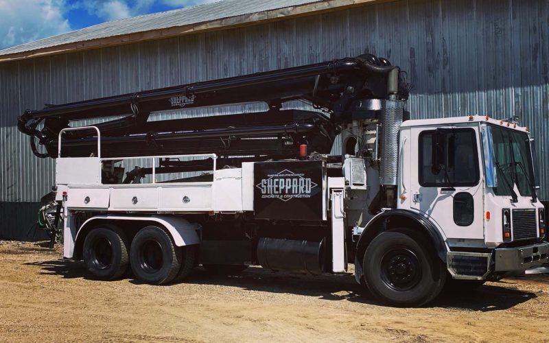 side view of concrete boom pump truck parked in front of garage, blue skies