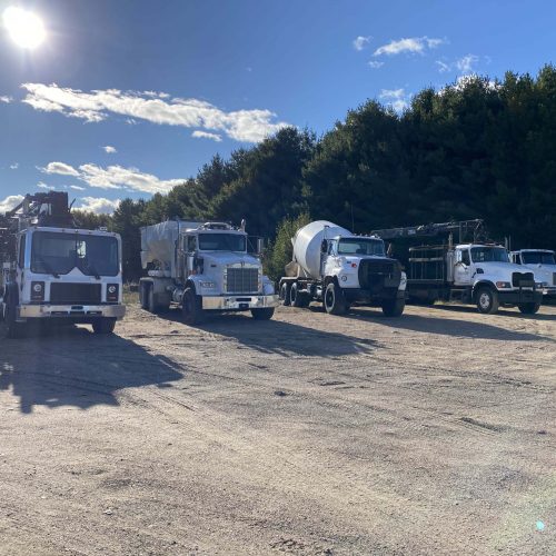 Sheppard concrete and construction fleet of heavy trucks, including gravel truck, concrete boom pump, Ready-Mix truck, Flatbed truck background is sunny summer day