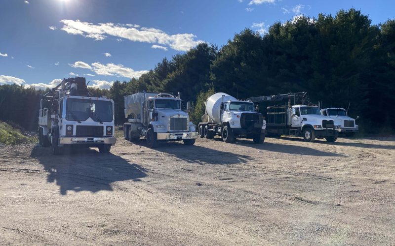 Sheppard concrete and construction fleet of heavy trucks, including gravel truck, concrete boom pump, Ready-Mix truck, Flatbed truck background is sunny summer day